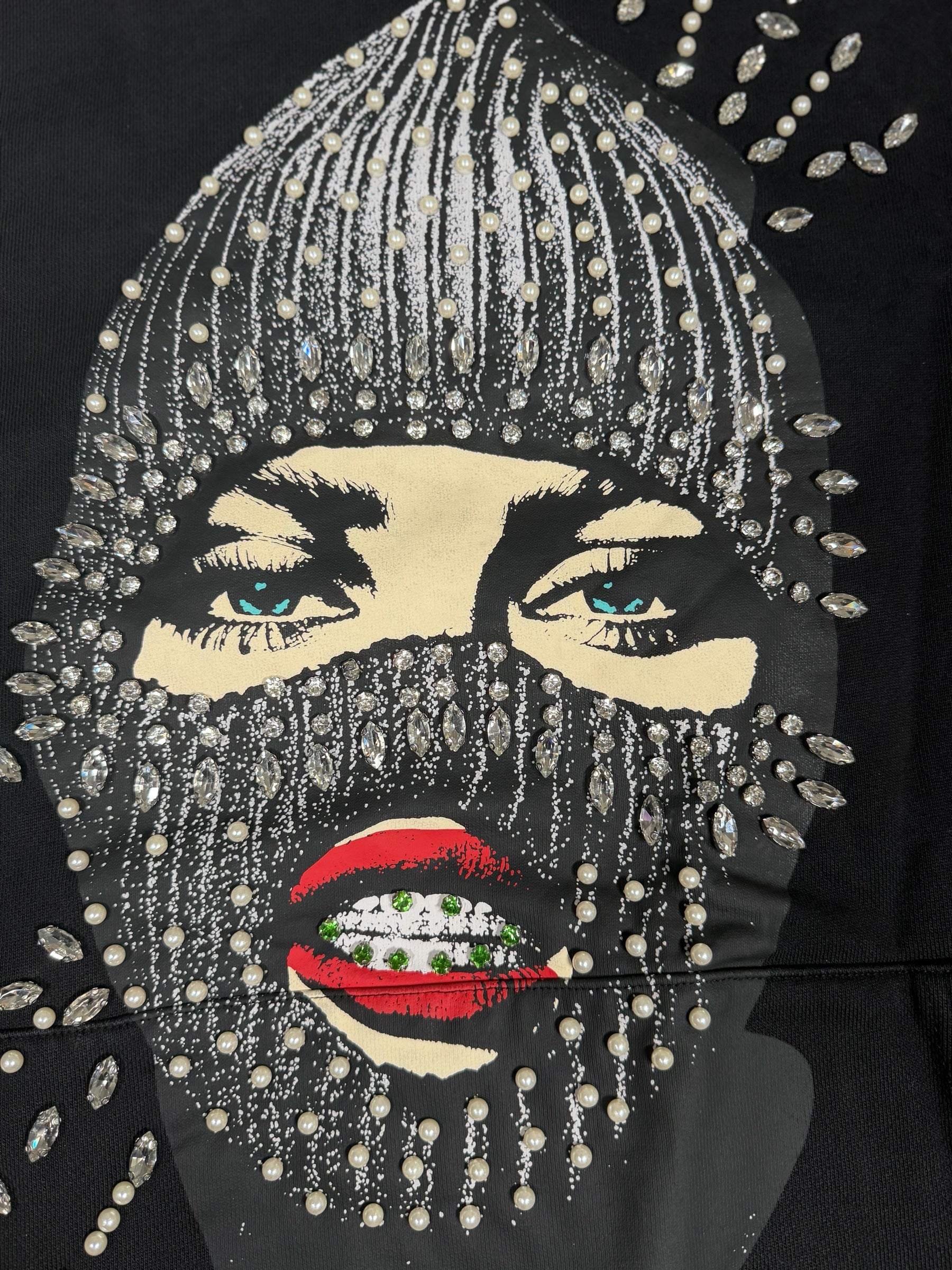 Dopetivity black hoodie featuring a graphic print of a masked face embellished with rhinestones and white pearls.